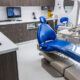 The image shows a well-furnished interior of a dentist's office. There is a chair for the patient and the doctor, lots of shelves and a desktop.