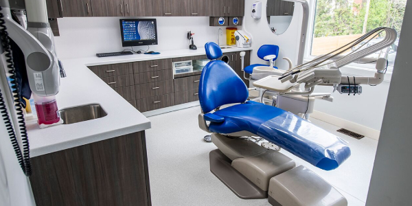 The image shows a well-furnished interior of a dentist's office. There is a chair for the patient and the doctor, lots of shelves and a desktop.